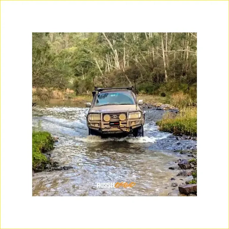 Brown rugged toyota landcruiser fj105 with premium rockarmor bullbar and rock sliders driving through shallow water