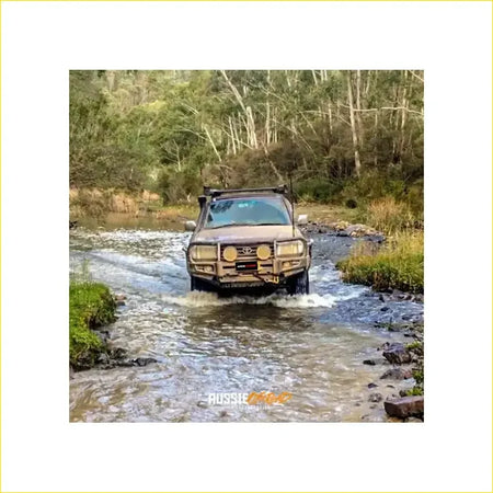 Brown rugged toyota landcruiser fj105 with premium rockarmor bullbar and rock sliders driving through shallow water